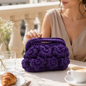Clutch viola Ametista con punto fiore appoggiata su tavolo elegante